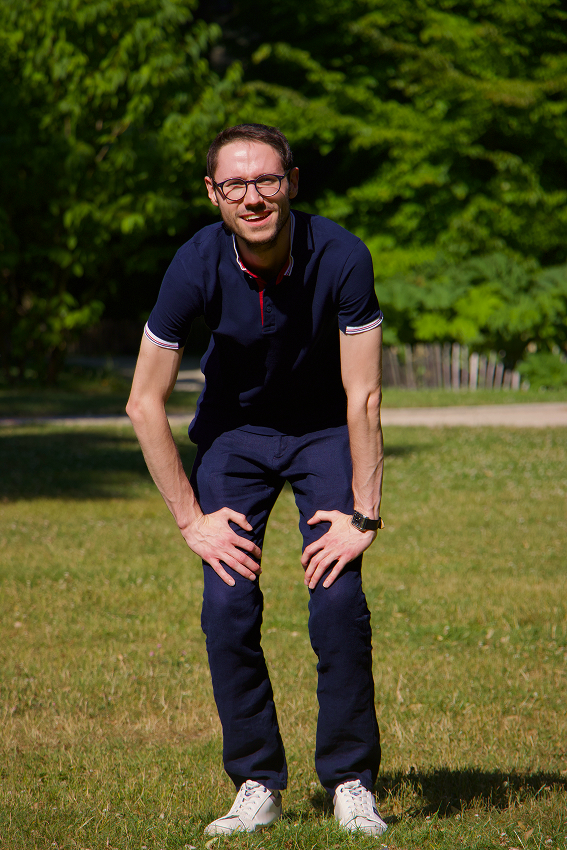 Maxime souriant en montagne, avec des batons de randonnée, dos à la montagne ensoleillée