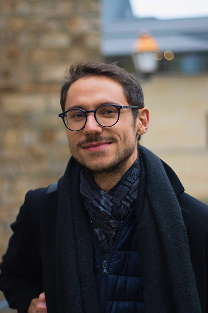 Maxime en train de marcher avec un léger sourire calme, fixant la caméra avec bienveillance