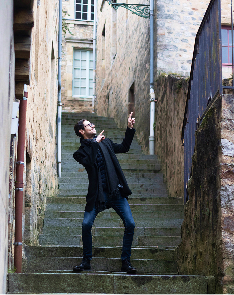 Maxime debout sur des marches pointant le ciel avec ses doigts