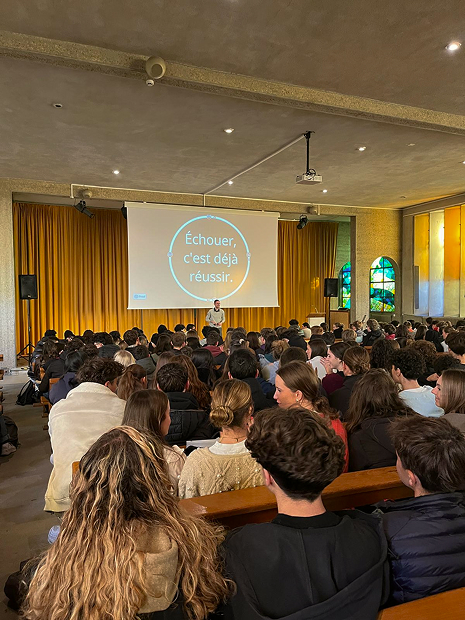 Maxime en conférence, debout dans une salle face à une audience de plus de 400 personnes