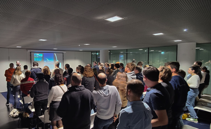 Maxime debout en conférence devant une audience de 100 personnes qui sont debouts